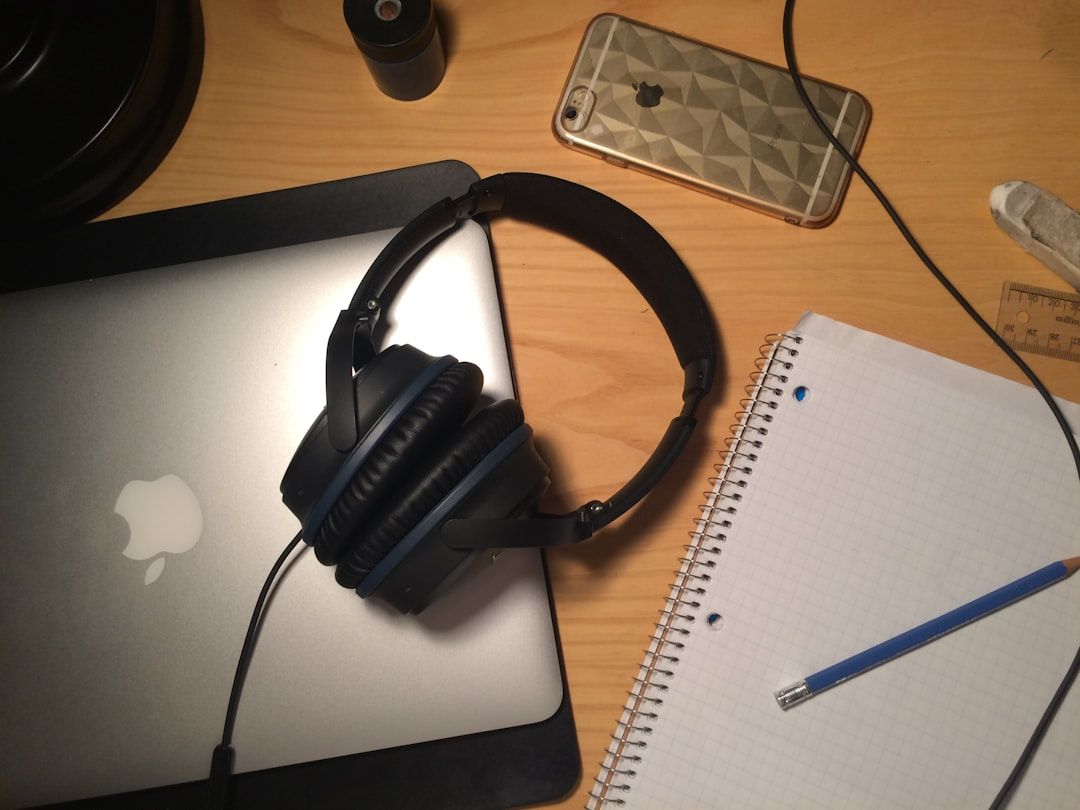 Överblick över skrivbord med laptop, hörlurar, telefon och anteckningsblock, relevant för podcastproduktion.